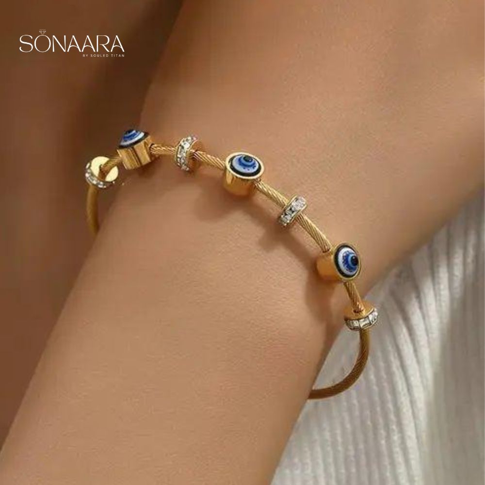 Gold bracelet with blue evil eye beads on a wrist, branded 'Sonaara'.