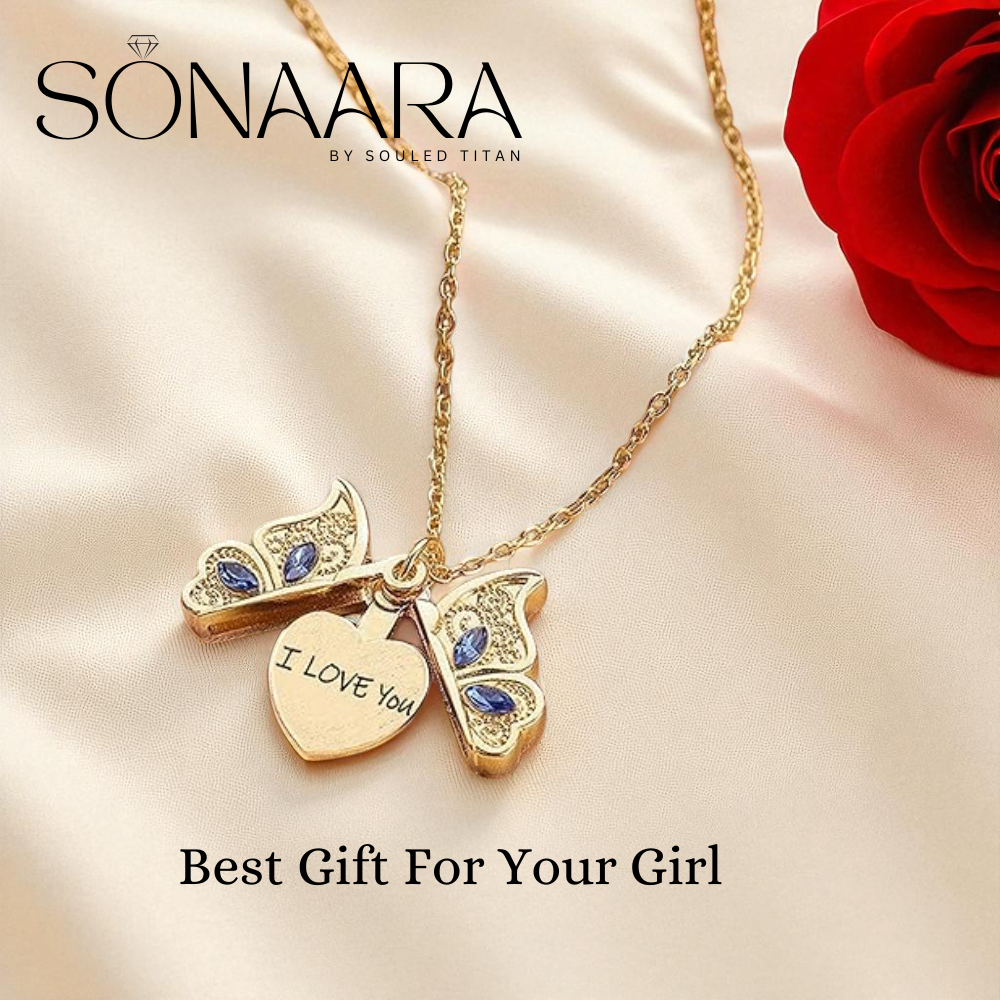 Gold necklace with heart and owl charms on a soft fabric background with a red rose.