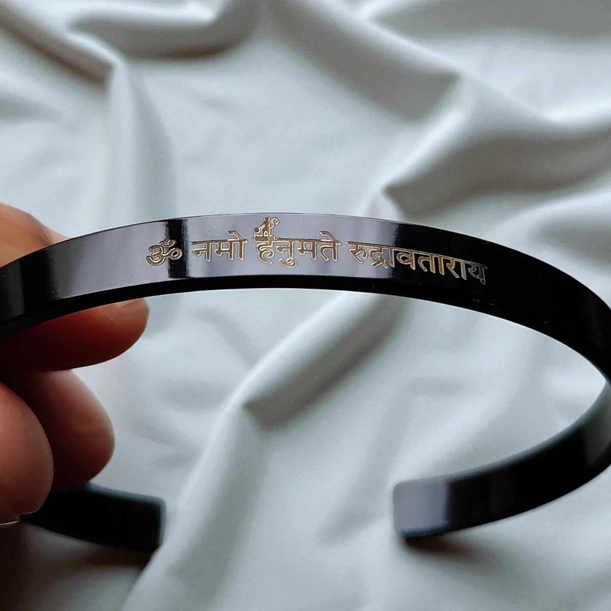 Black bracelet with Hanuman mantra text held by a hand on a white fabric background