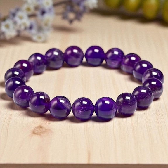 Purple Amethyst bracelet on a wooden surface with blurred flowers in the background