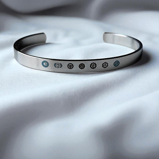 Silver 7 chakra bracelet with engraved symbols on a white fabric background