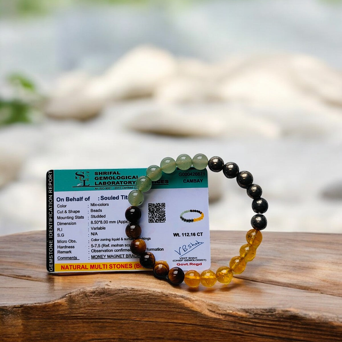 Money Magnet bracelet on a card with gemstone lab report, placed on a wooden surface with a blurred natural background.