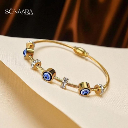 Gold bracelet with blue stones and evil eye beads on a beige surface, branded 'Sonaara'.