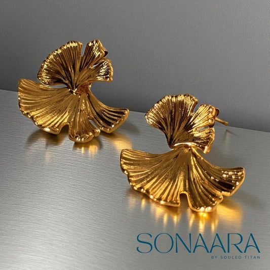Gold leaf-shaped earrings on a reflective surface with 'Sonaara' branding.