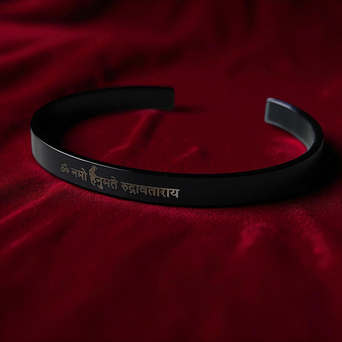 Black bracelet with engraved Hanuman mantra on a red fabric background